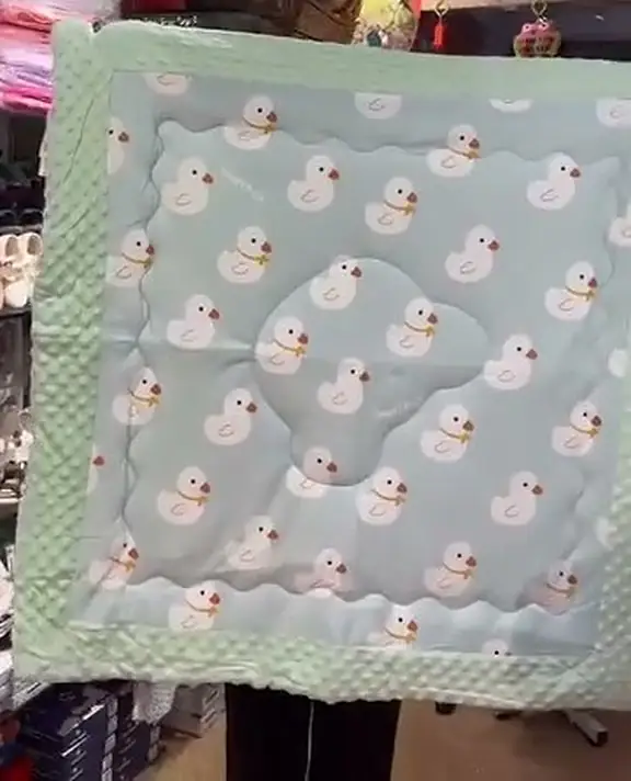A pale green quilted muslin blanket printed all over with small white ducks, held up in the shop.